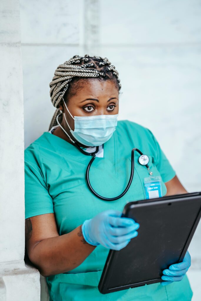Female nurse in scrubs and mask reviewing patient data on a tablet.